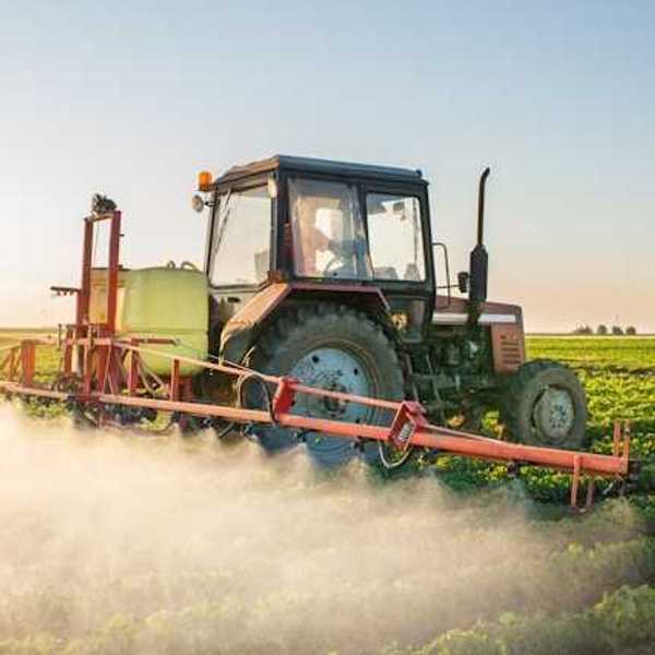 A tractor driving through a farm field applying pesticides