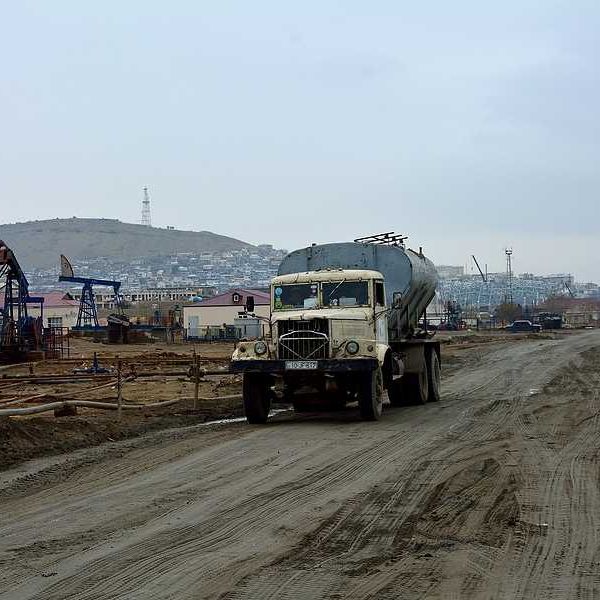 A truck drives down a muddy road next to aging oil pumps