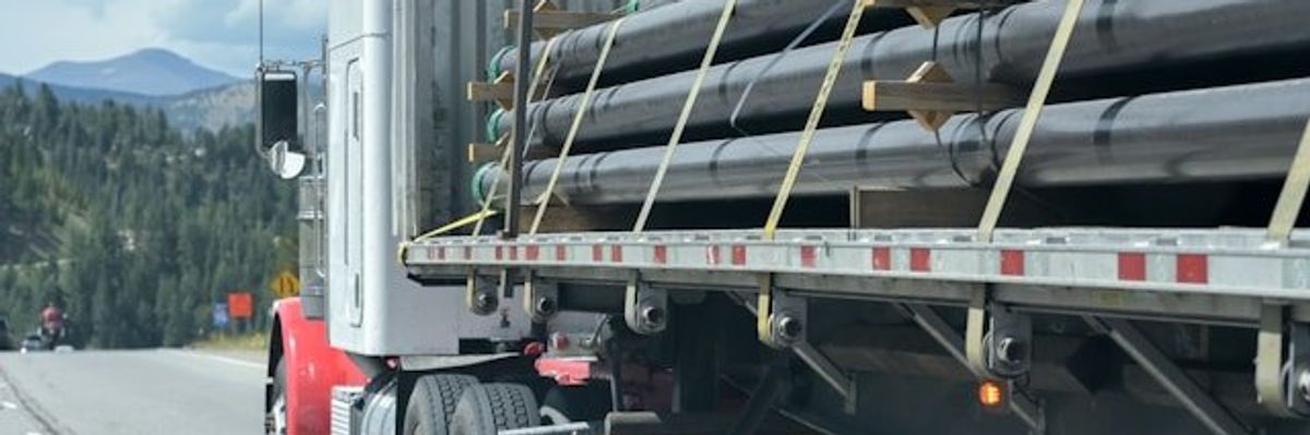 A truck with rows of pipeline tied to the flatbed.