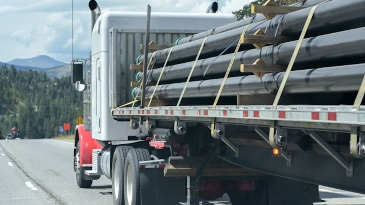 A truck with rows of pipeline tied to the flatbed.