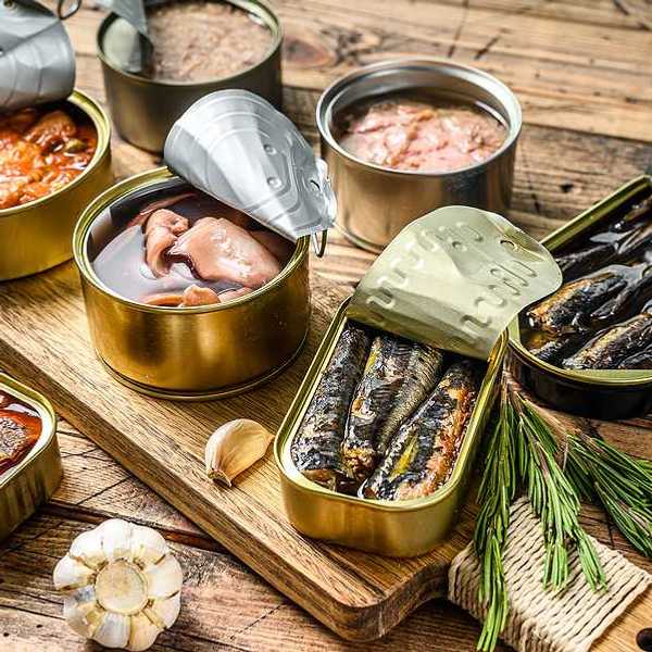 A variety of canned fish in metal cans with the lids open on a wood surface