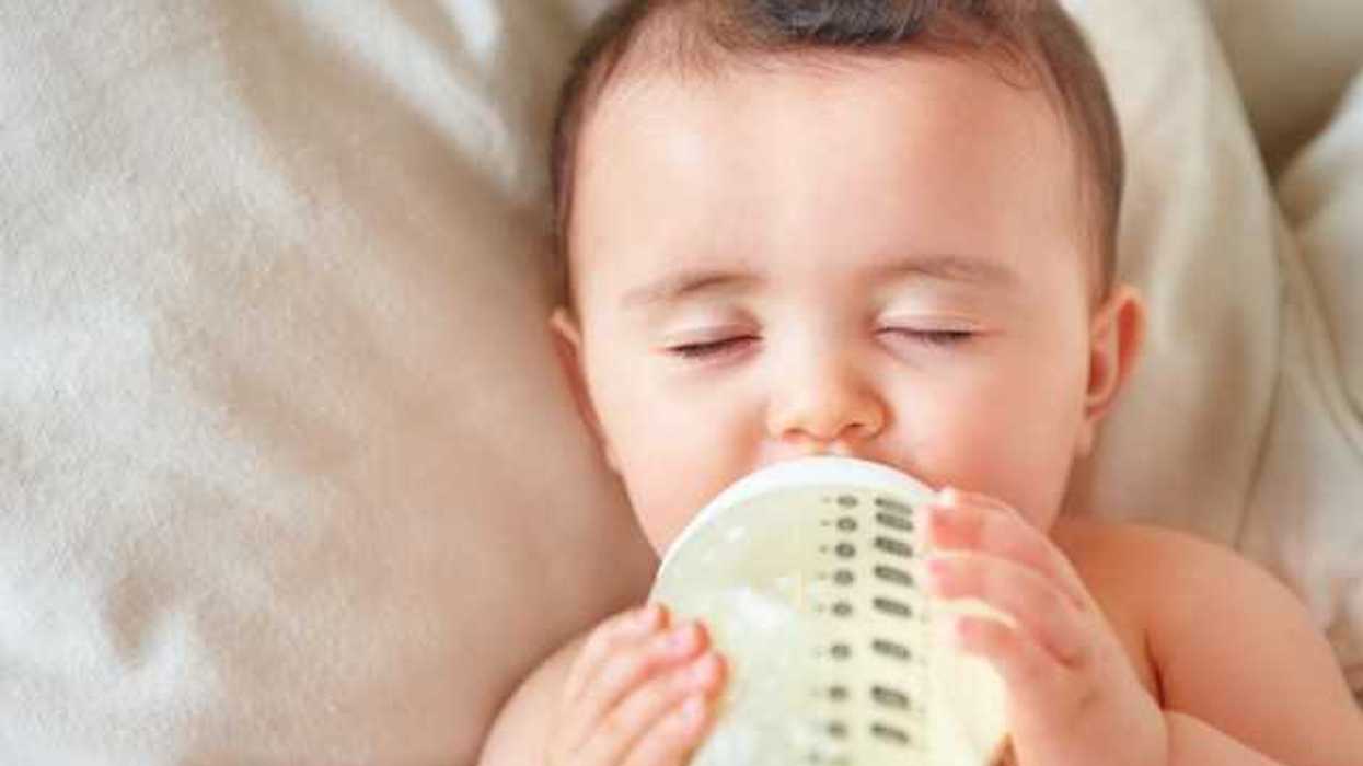 A view of a baby lying on a blanket while drinking from a bottle