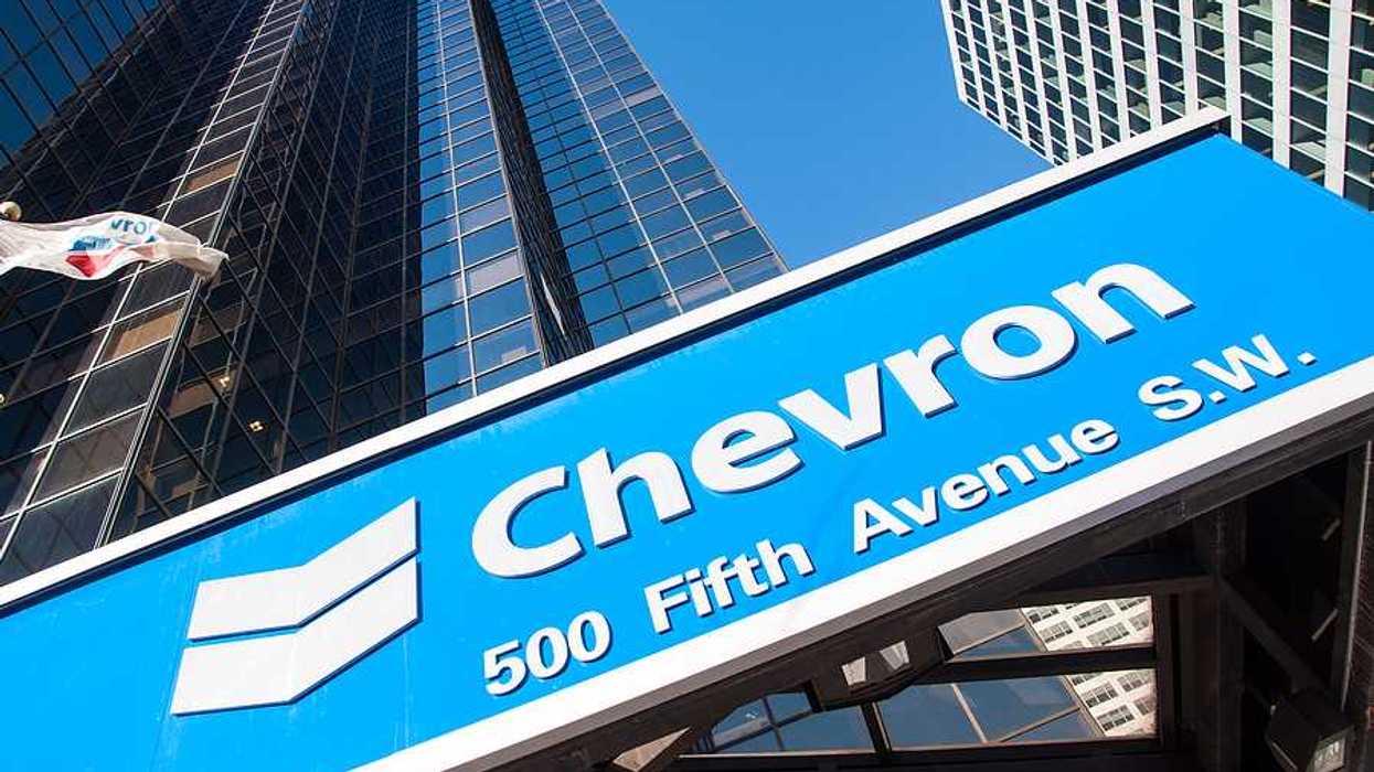 A view of a blue Chevron sign with rising sky scrapers behind it