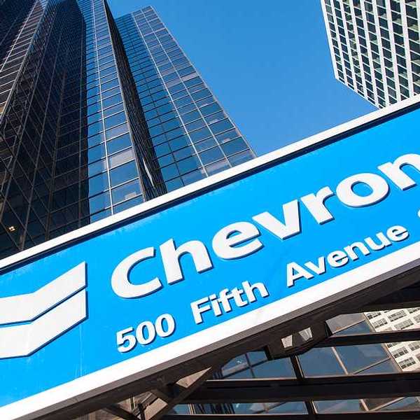 A view of a blue Chevron sign with rising sky scrapers behind it