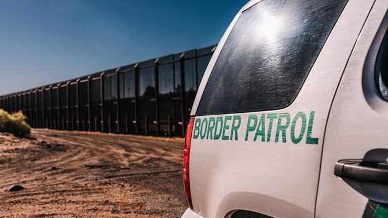 A view of a Border Patrol vehicle next to a tall metal border wall
