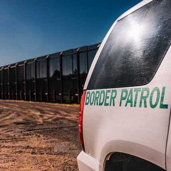 A view of a Border Patrol vehicle next to a tall metal border wall