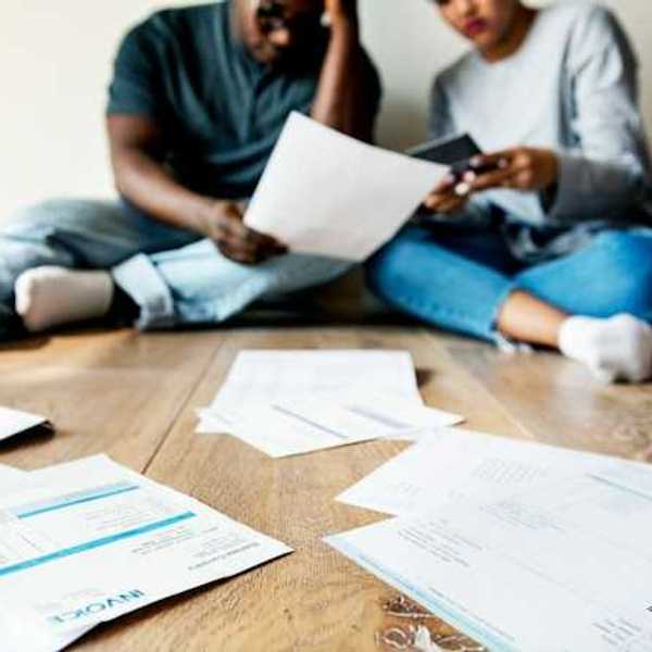 A view of a couple sitting on the floor looking through bills