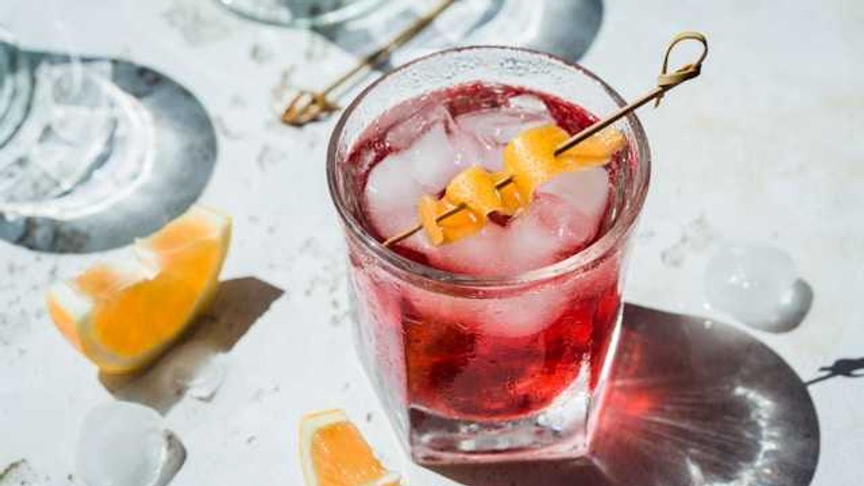 A view of a dark pink cocktail with an orange twist in the top