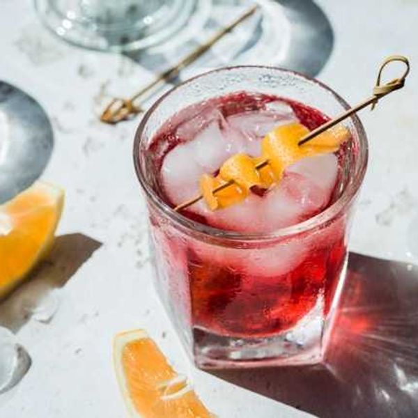 A view of a dark pink cocktail with an orange twist in the top