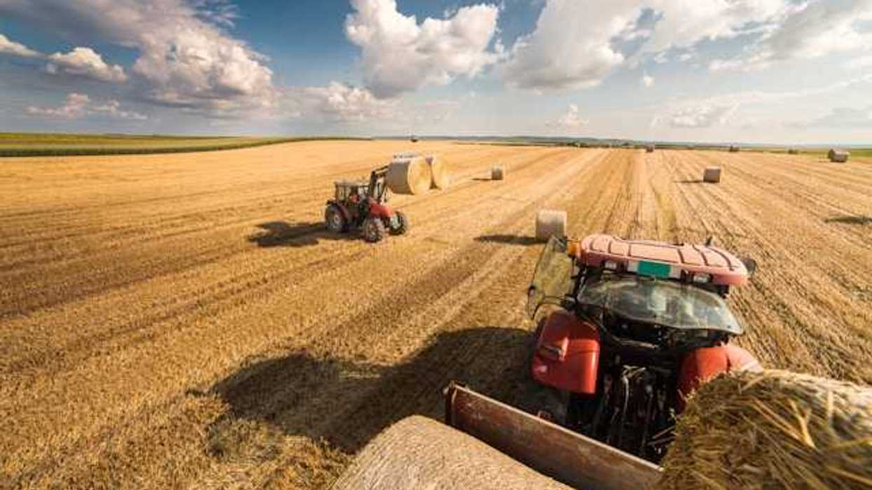 A view of a farm field being harvested by two farm tractors