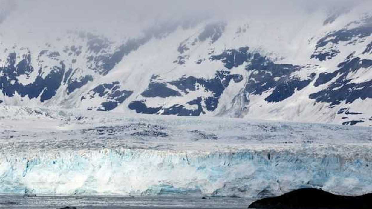 A view of a glacier with snow covered mountains behind it
