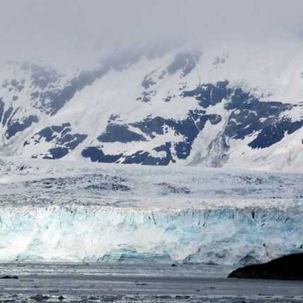 A view of a glacier with snow covered mountains behind it