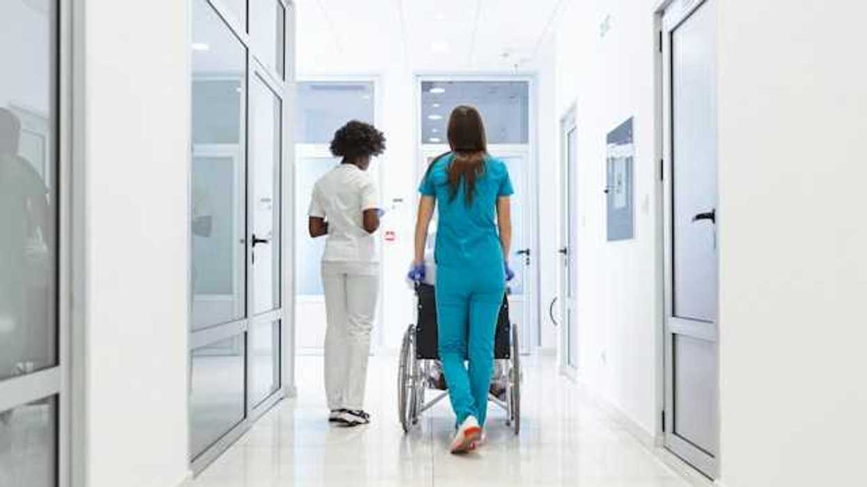 A view of a hospital corridor with two nurses wheeling a patient toward a room