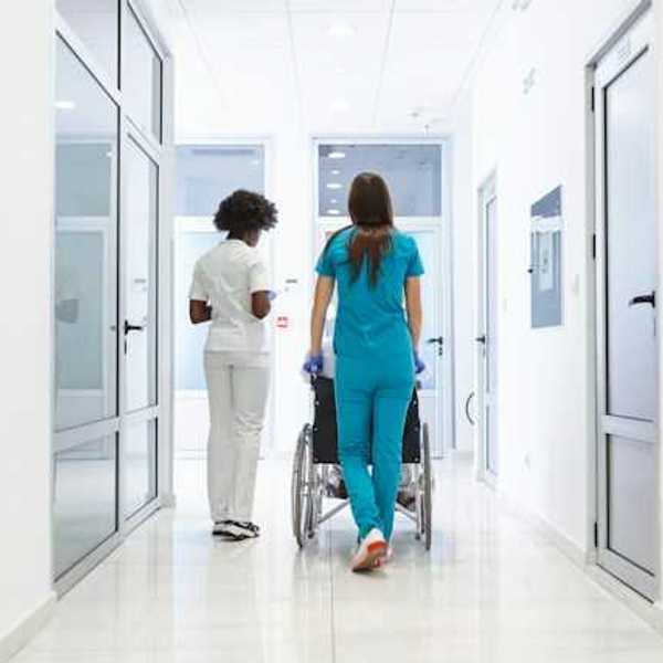 A view of a hospital corridor with two nurses wheeling a patient toward a room