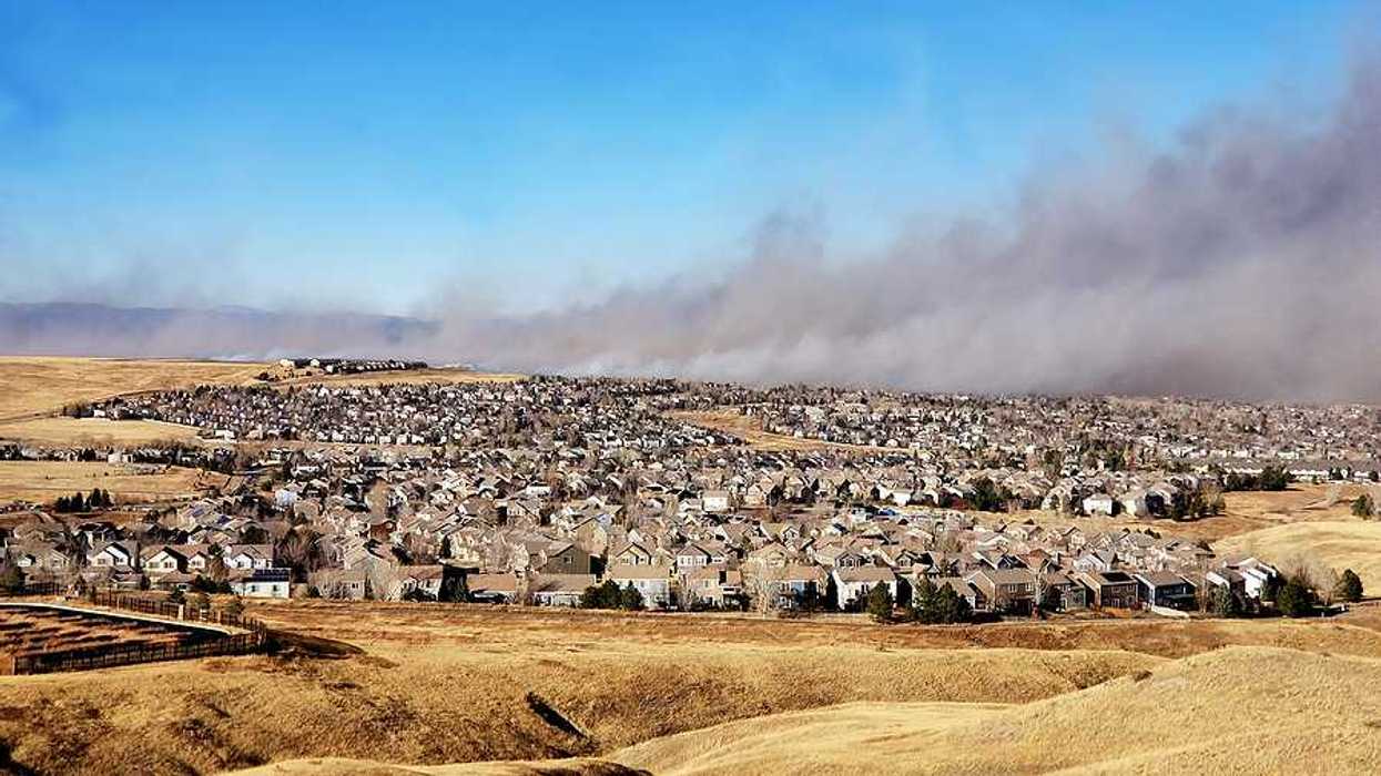 A view of a housing development with a wildfire and smoke in the background