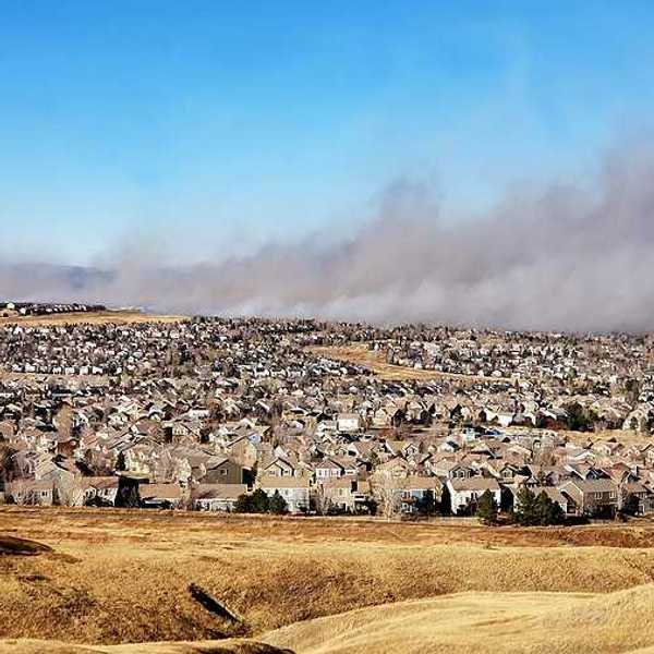 A view of a housing development with a wildfire and smoke in the background