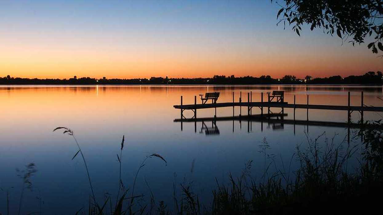A view of a lake at sunset with a dock stretching out over the water