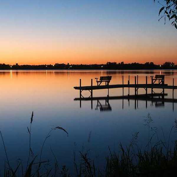 A view of a lake at sunset with a dock stretching out over the water