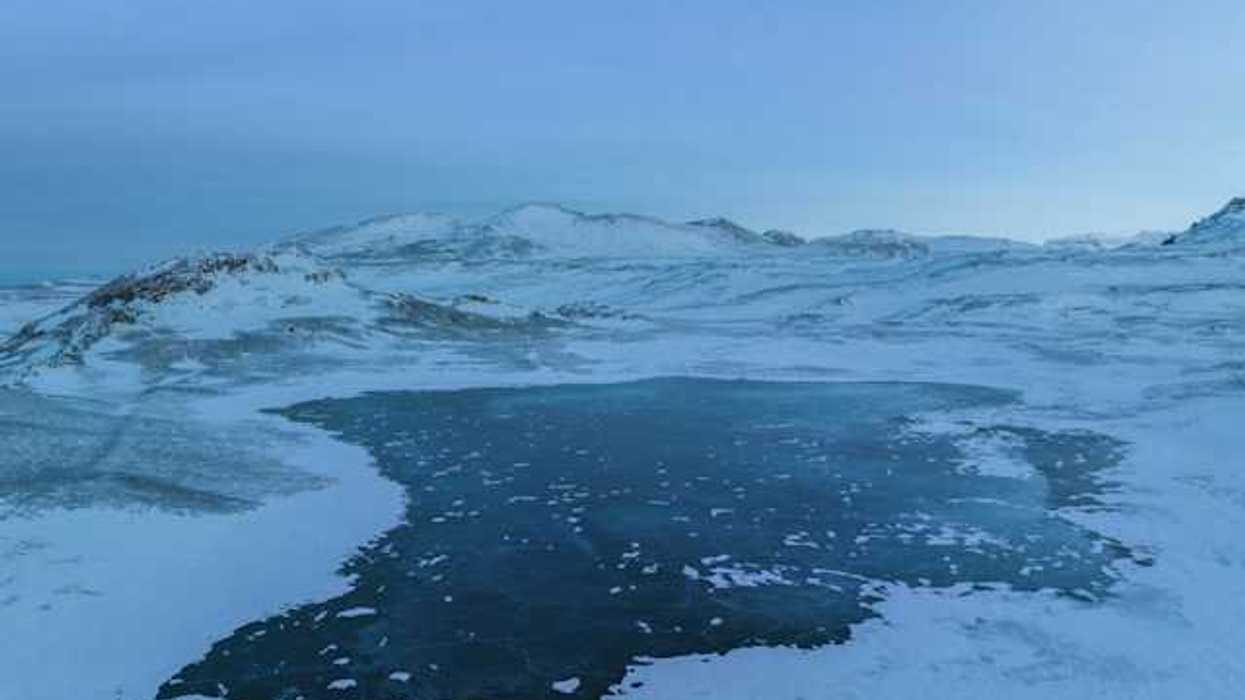 A view of a lake surrounded by ice and snow with mountains in the background