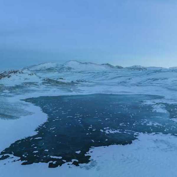 A view of a lake surrounded by ice and snow with mountains in the background
