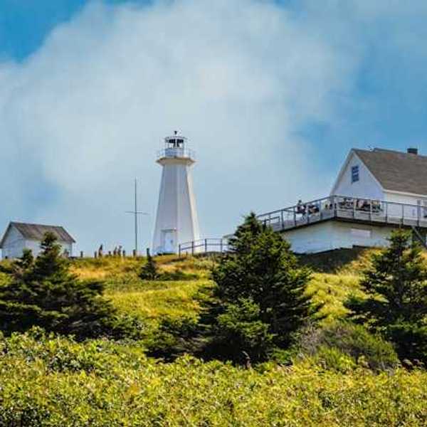 A view of a lighthouse from below a grassy hill