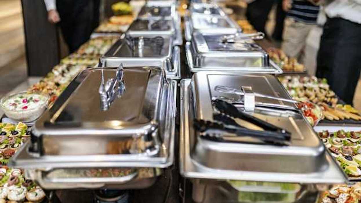 A view of a long buffet table with silver trays and plates of food
