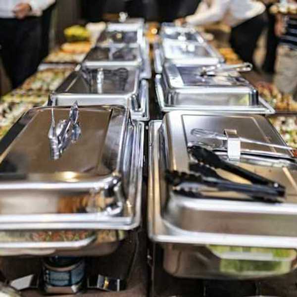 A view of a long buffet table with silver trays and plates of food