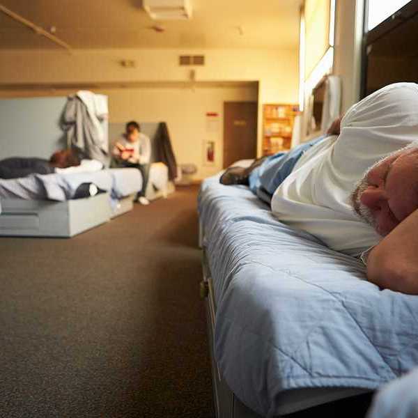 A view of a man lying on a bed in a homeless shelter