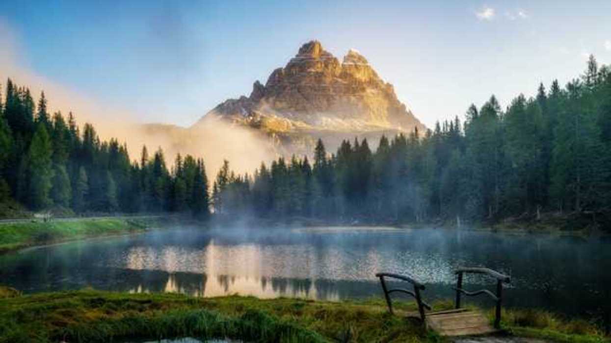 A view of a mountain peak with a small lake and forest trees in the foreground