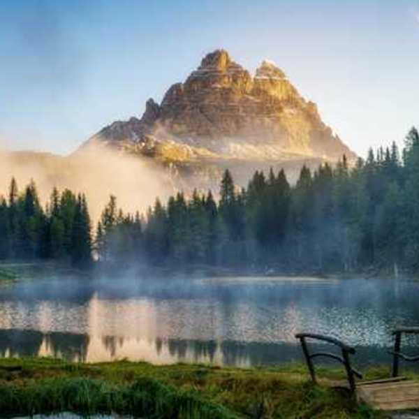 A view of a mountain peak with a small lake and forest trees in the foreground