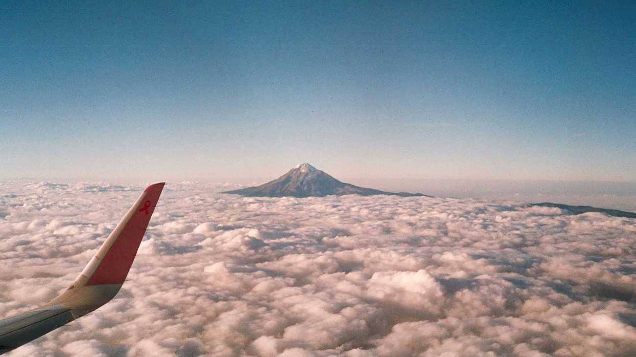 A view of a mountain poking out from the clouds, as seen from an airplane window.