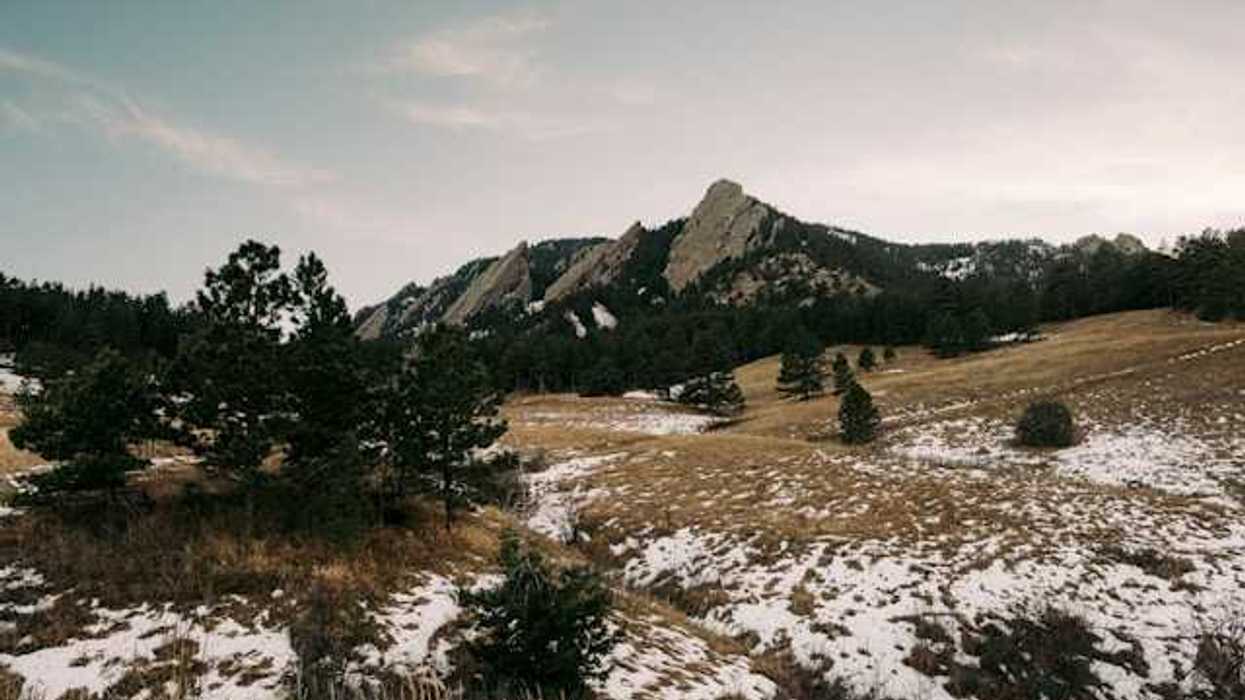 A view of a mountain range with sparse snow in the foreground