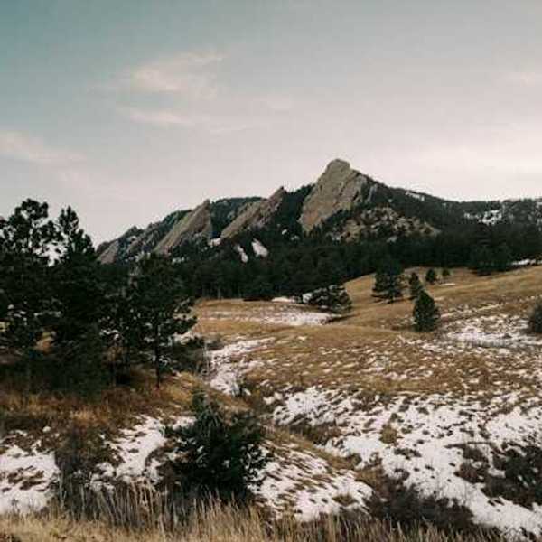 A view of a mountain range with sparse snow in the foreground