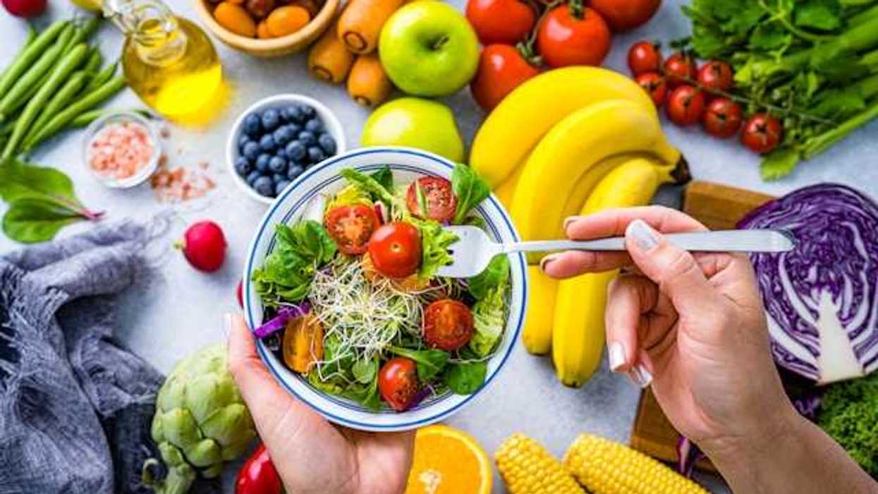 A view of a person eating a salad, surrounded by fruits and vegetables on a table