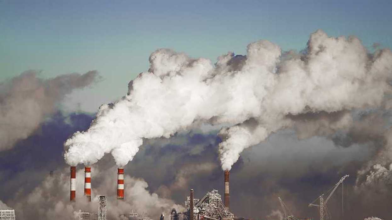 A view of a power plant with red and white smokestacks and pollution billowing into the sky