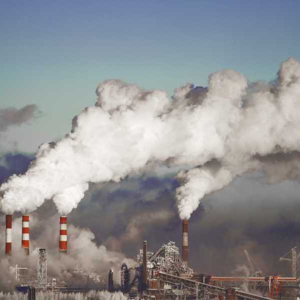 A view of a power plant with red and white smokestacks and pollution billowing into the sky