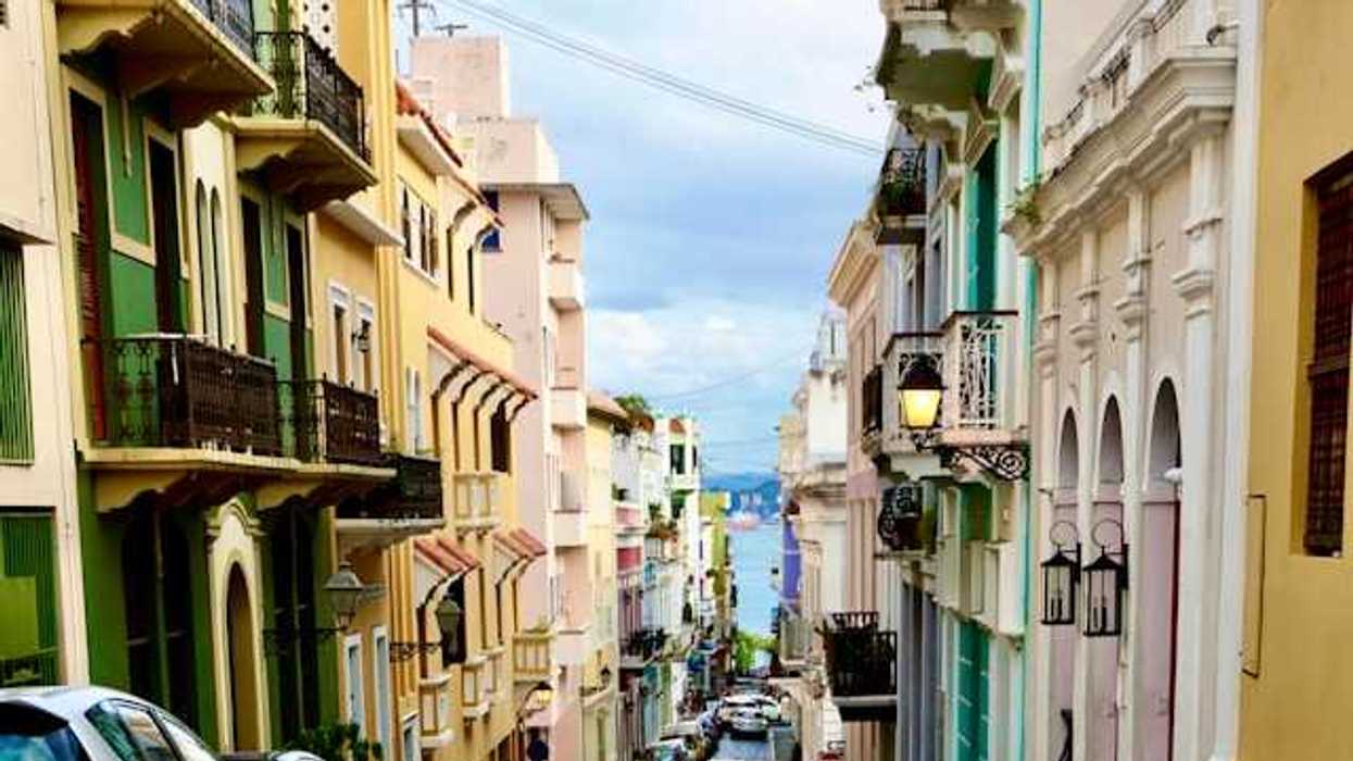 A view of a Puerto Rican street with multicolored buildings and cars and the ocean in the far distance