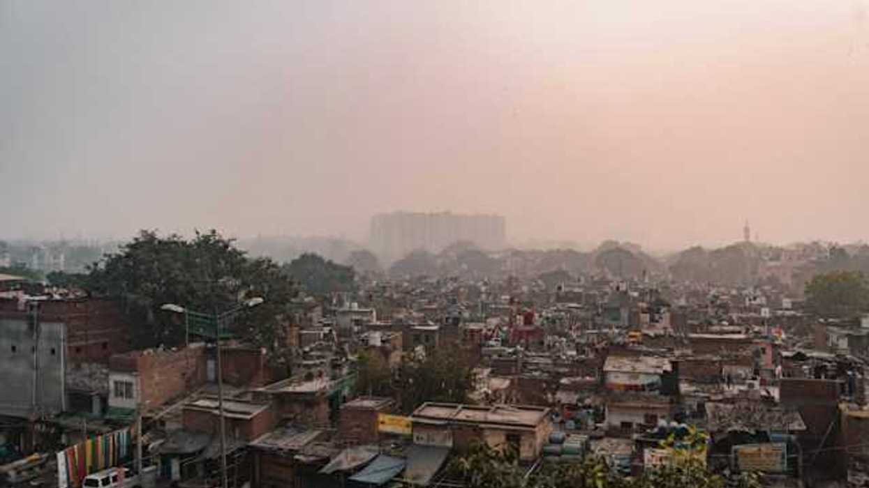 A view of a shantytown with larger buildings in the distance and smog in the air