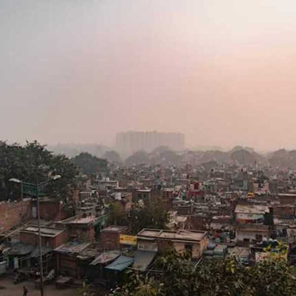 A view of a shantytown with larger buildings in the distance and smog in the air