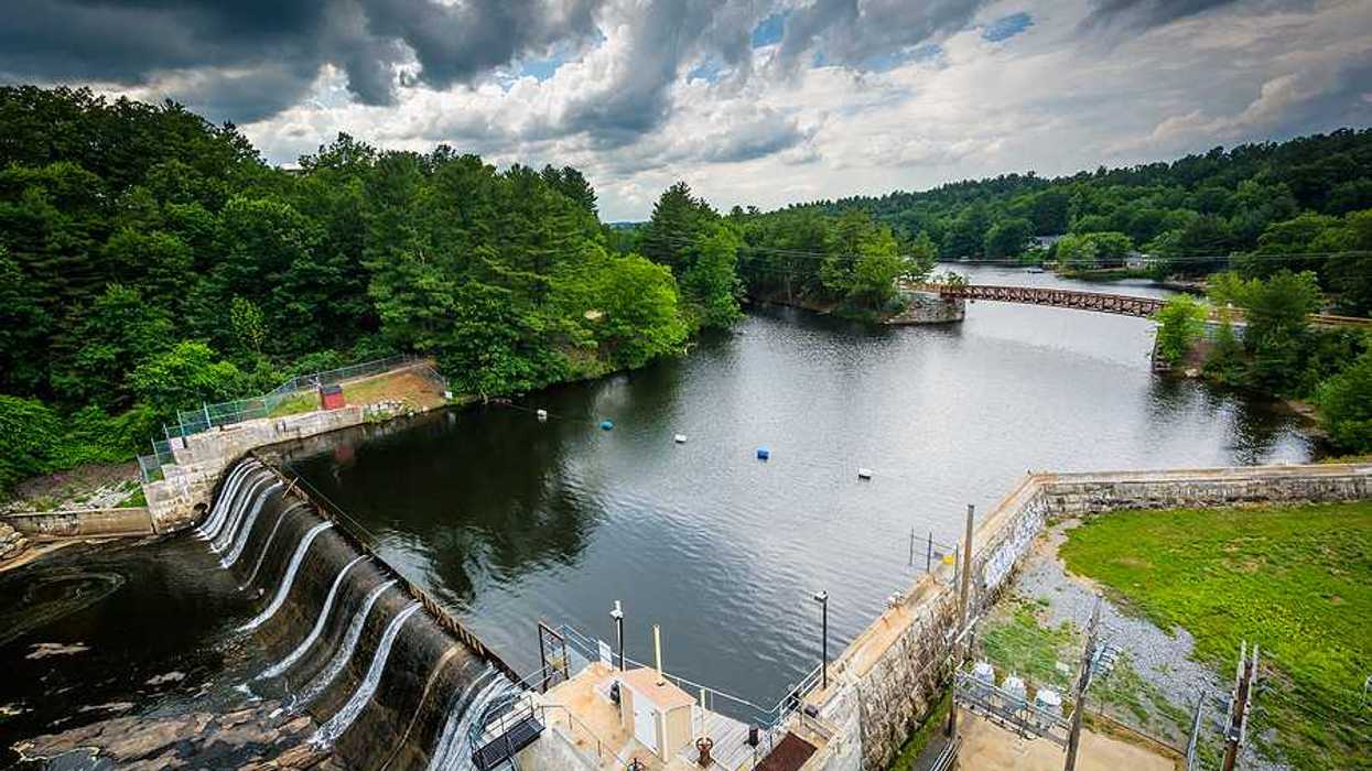 A view of a small dam with green trees and a small bridge in the background