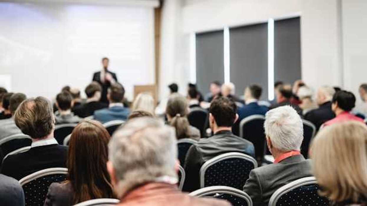 A view of a speaker at a conference from the back of the room