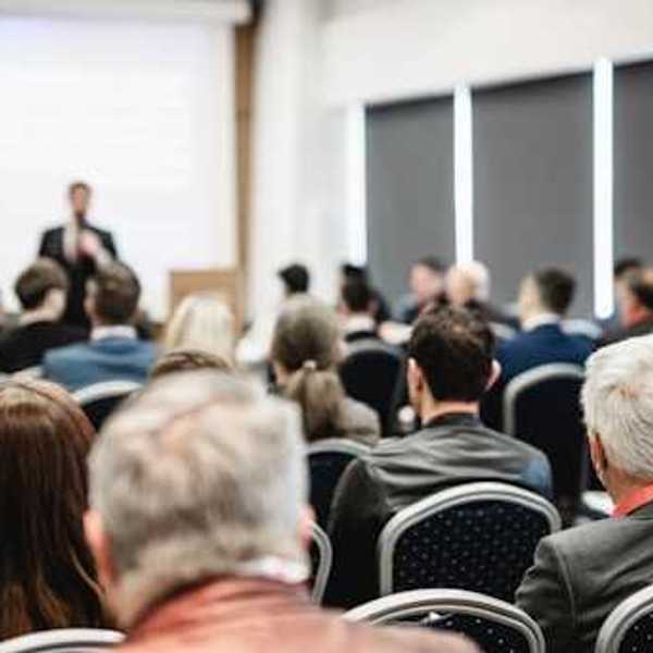 A view of a speaker at a conference from the back of the room