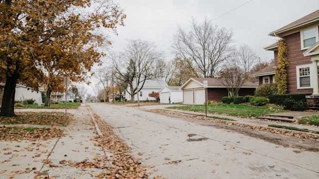 A view of a suburban street with leaves on the sidewalks
