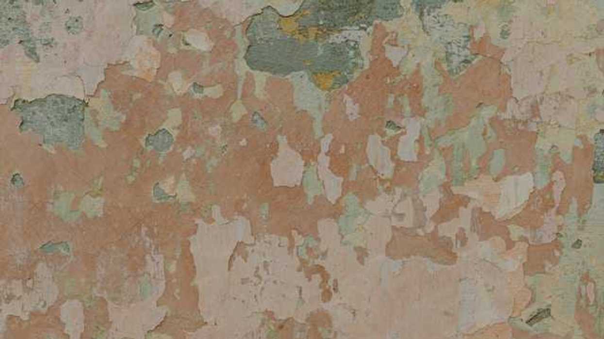 A view of a wall with various colors of paint peeling from it