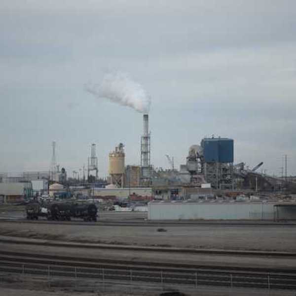 A view of an industrial factory with smoke rising out of a smokestack