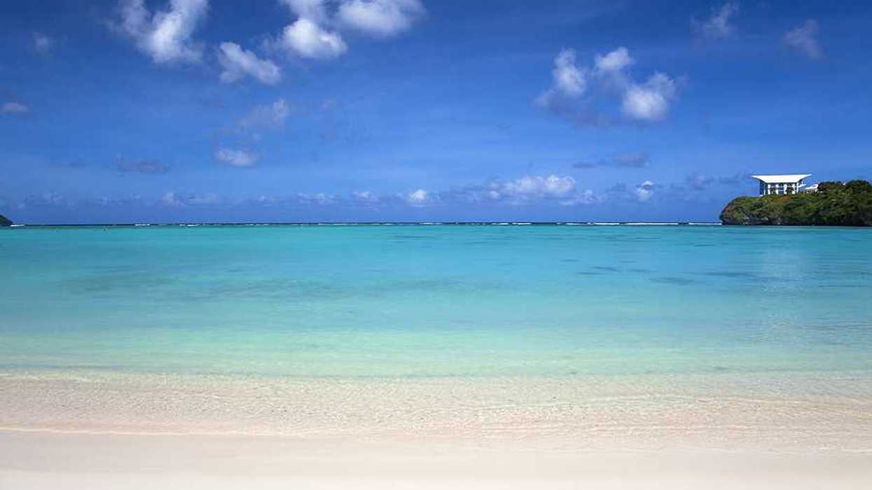 A view of aqua water and a white sand beach under a blue sky