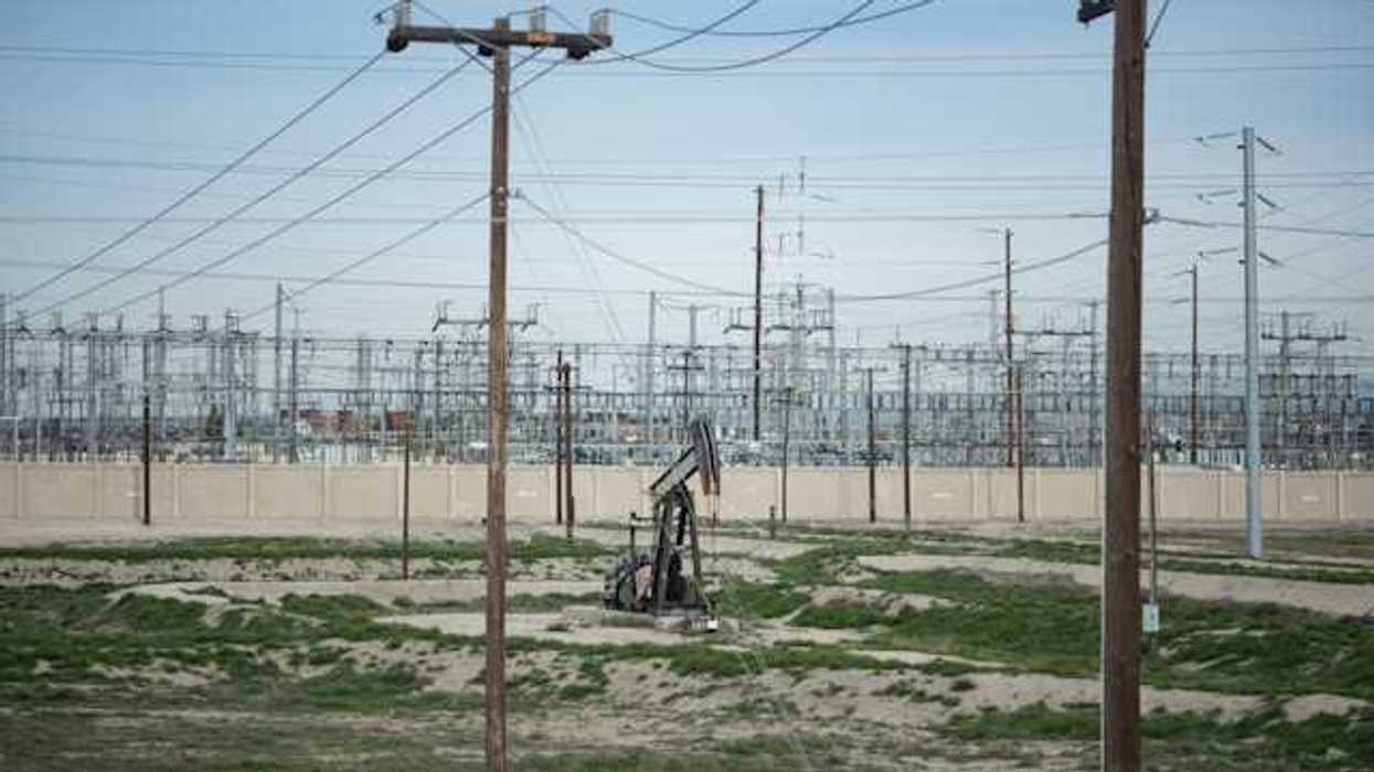 A view of energy lines with a small oil pump jack in a sandy field