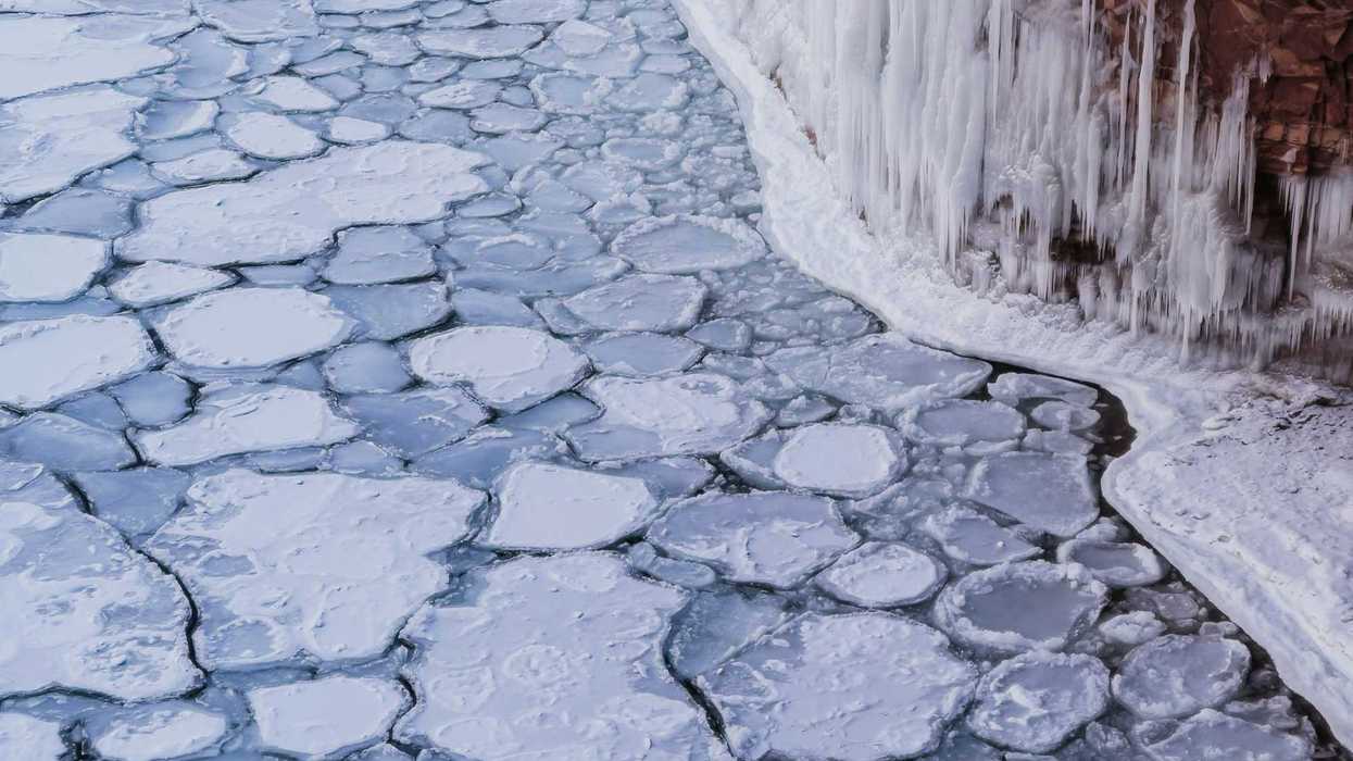 A view of ice-covered water with icicles forming on a nearby cliff