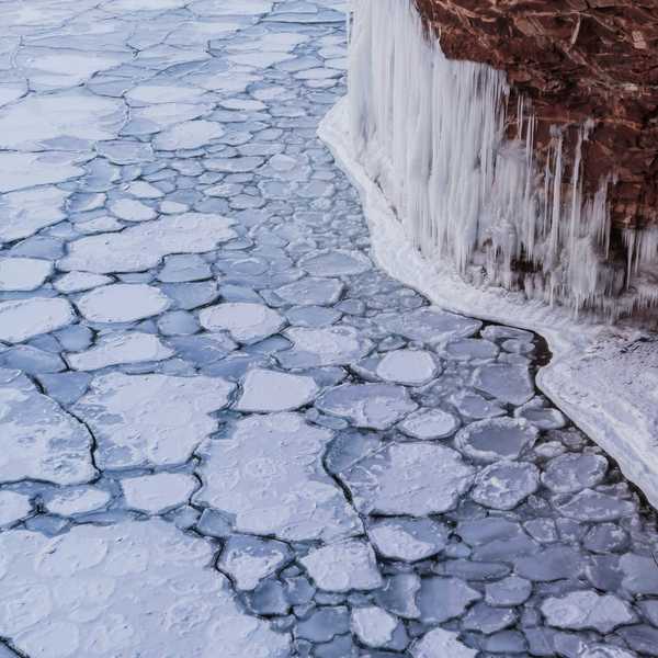 A view of ice-covered water with icicles forming on a nearby cliff