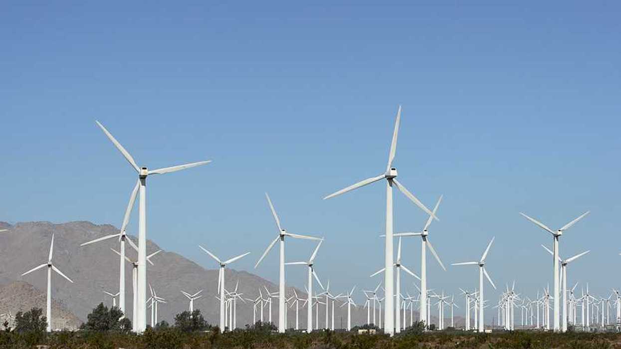 A view of multiple white wind turbines with dry mountains in the background